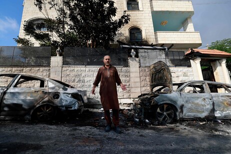 Homem diante de carros queimados por colonos israelenses em Jit