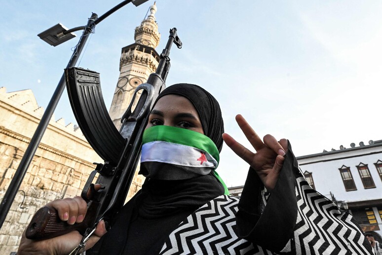 Mulher mascarada celebra queda de Assad diante de mesquita em Damasco, capital da Síria © ANSA/AFP