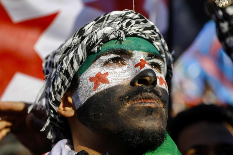 Homem pinta rosto com cores de bandeira de rebeldes para celebrar queda de Assad © ANSA/AFP